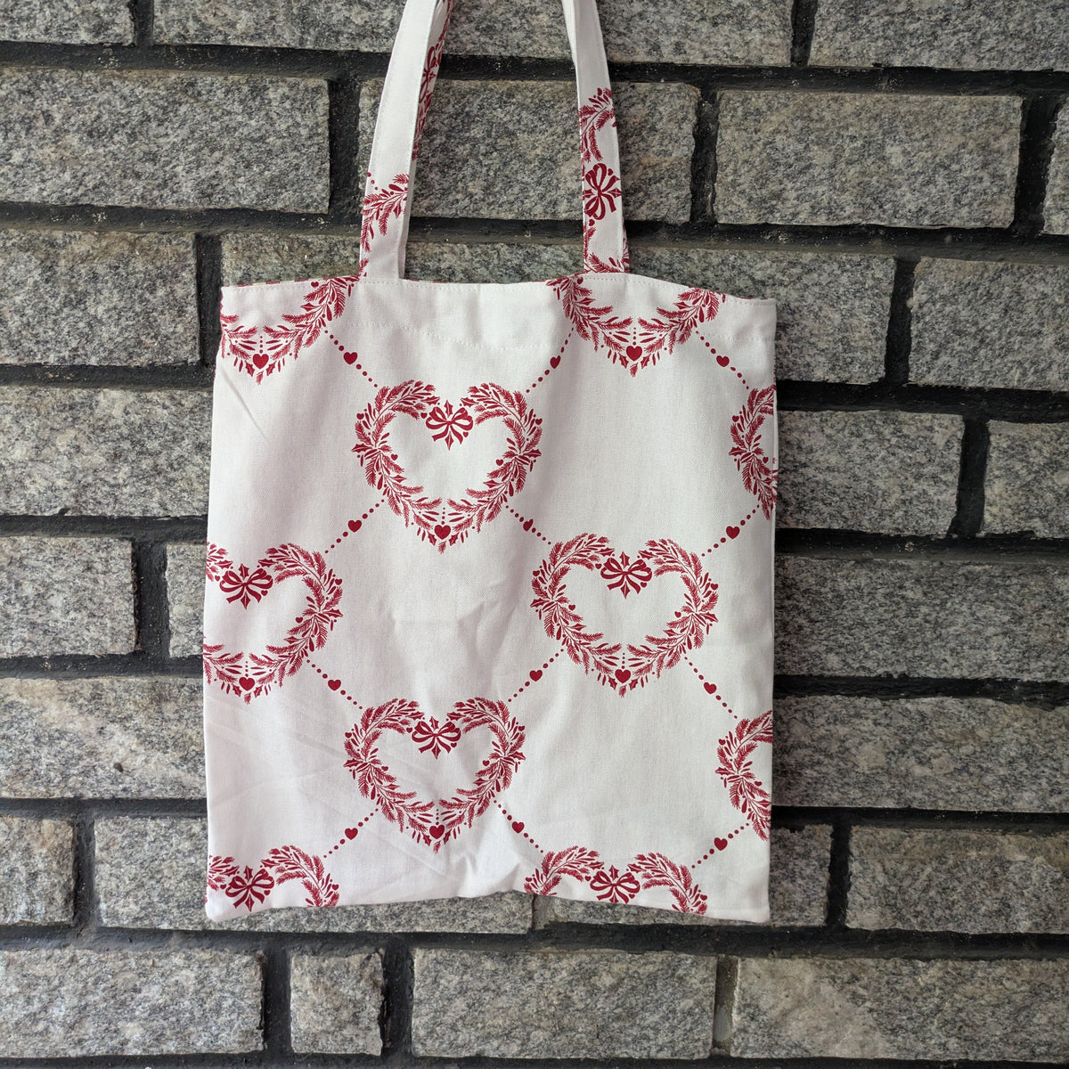 Tote bag with red heart pattern hanging on a brick wall