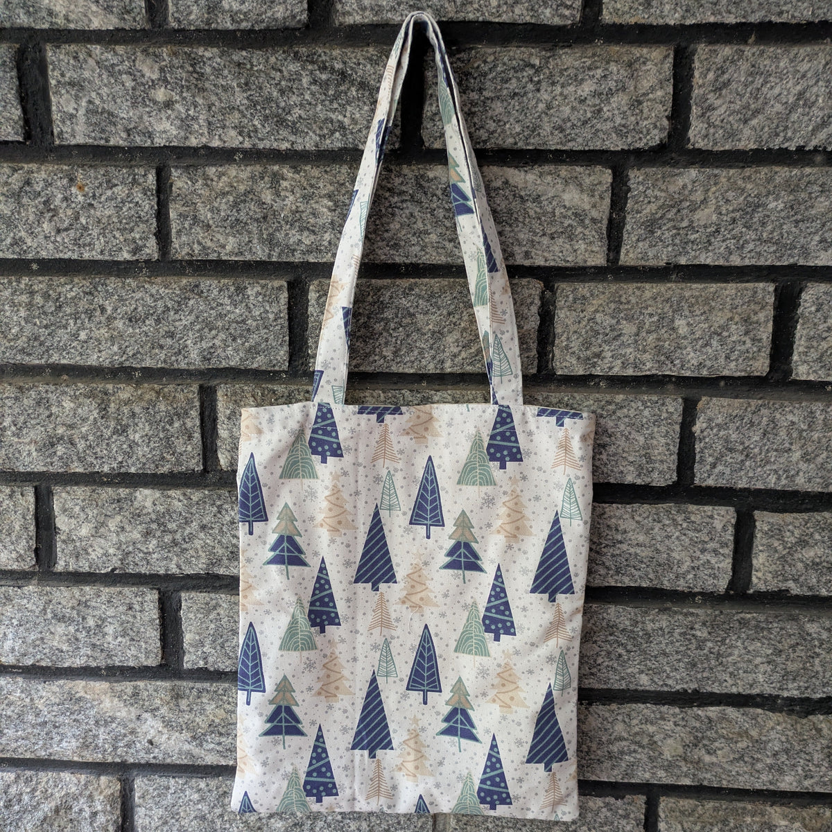 Tote bag with tree pattern hanging against a brick wall