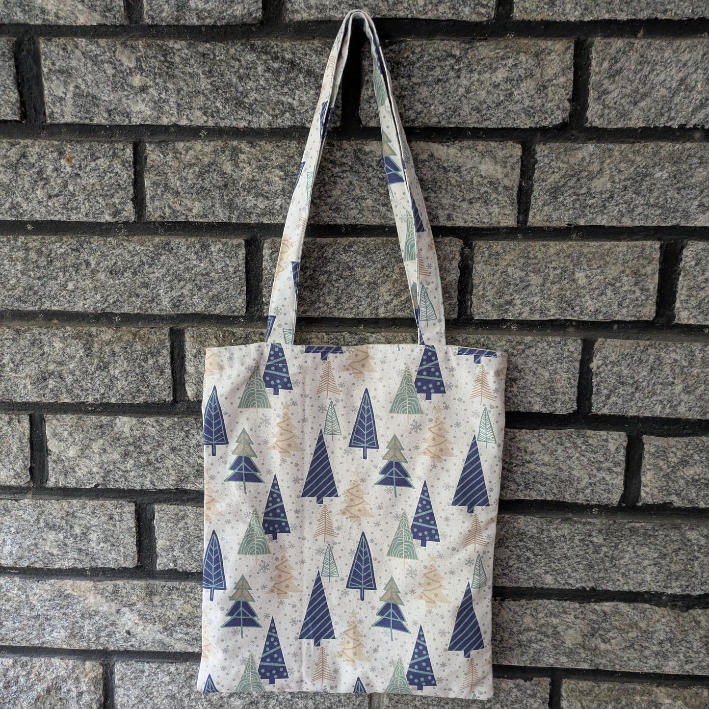 Tote bag with tree pattern hanging against a brick wall