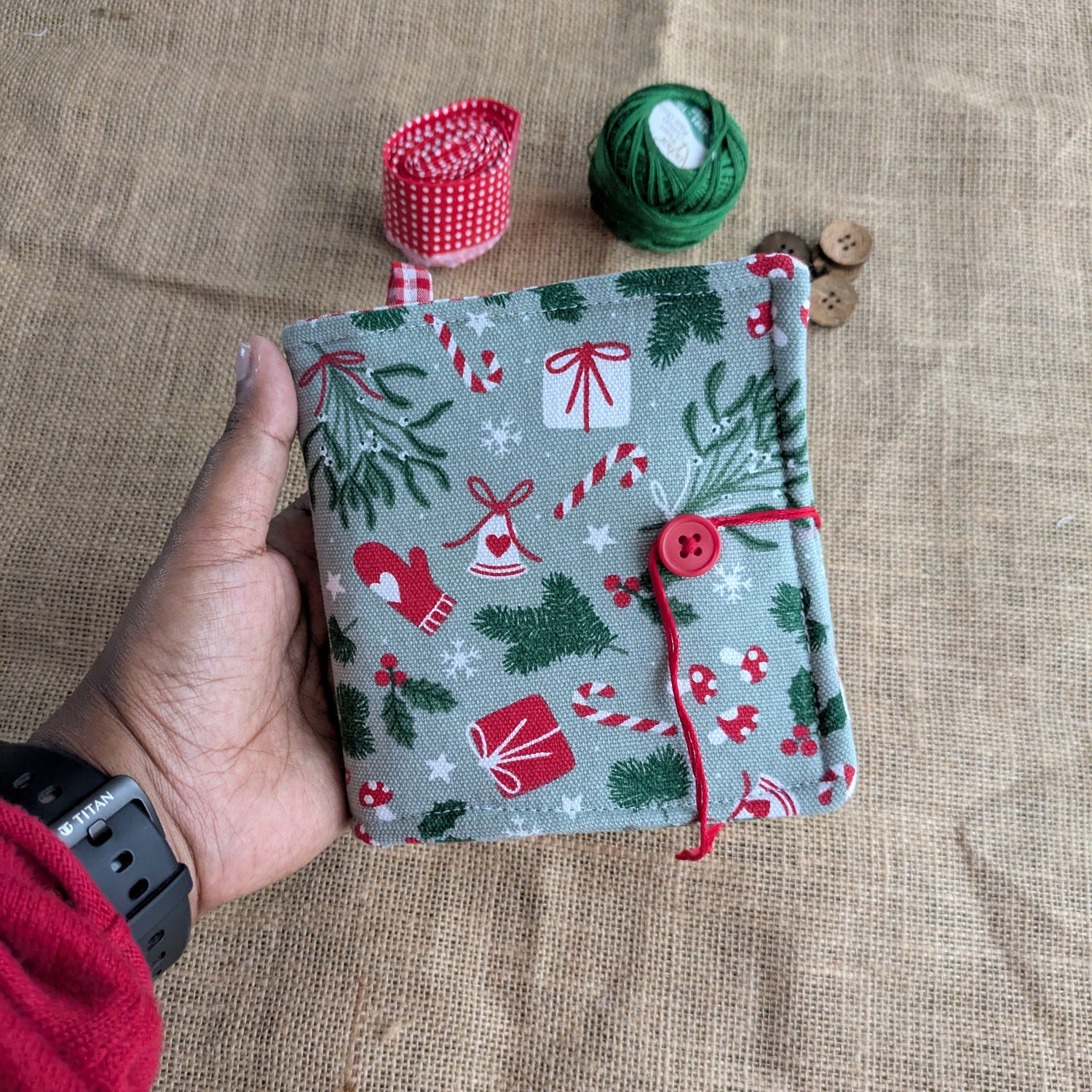 Hand holding a small fabric pouch with Christmas patterns on a textured surface