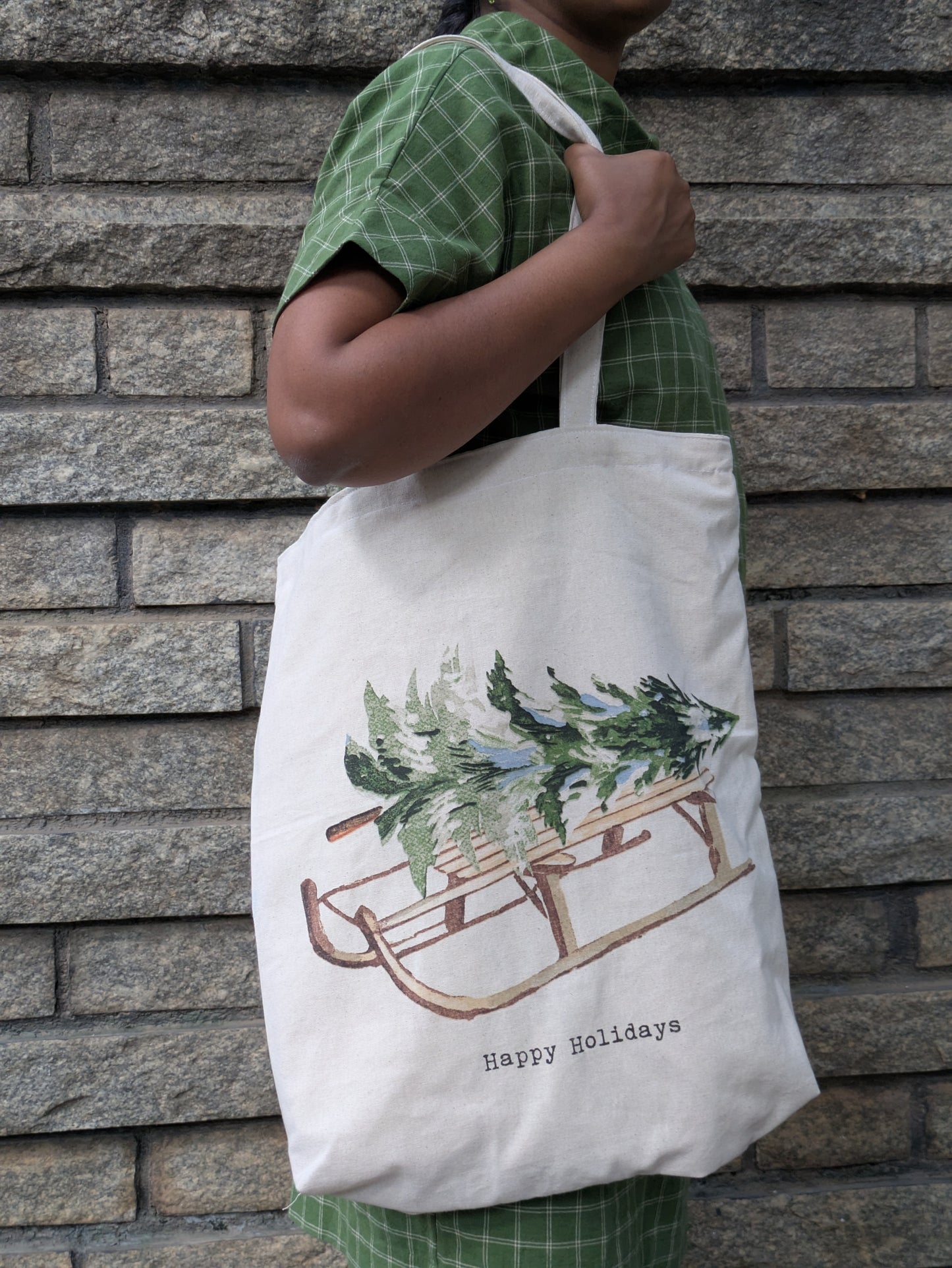 Person holding a tote bag with a Christmas design against a brick wall.