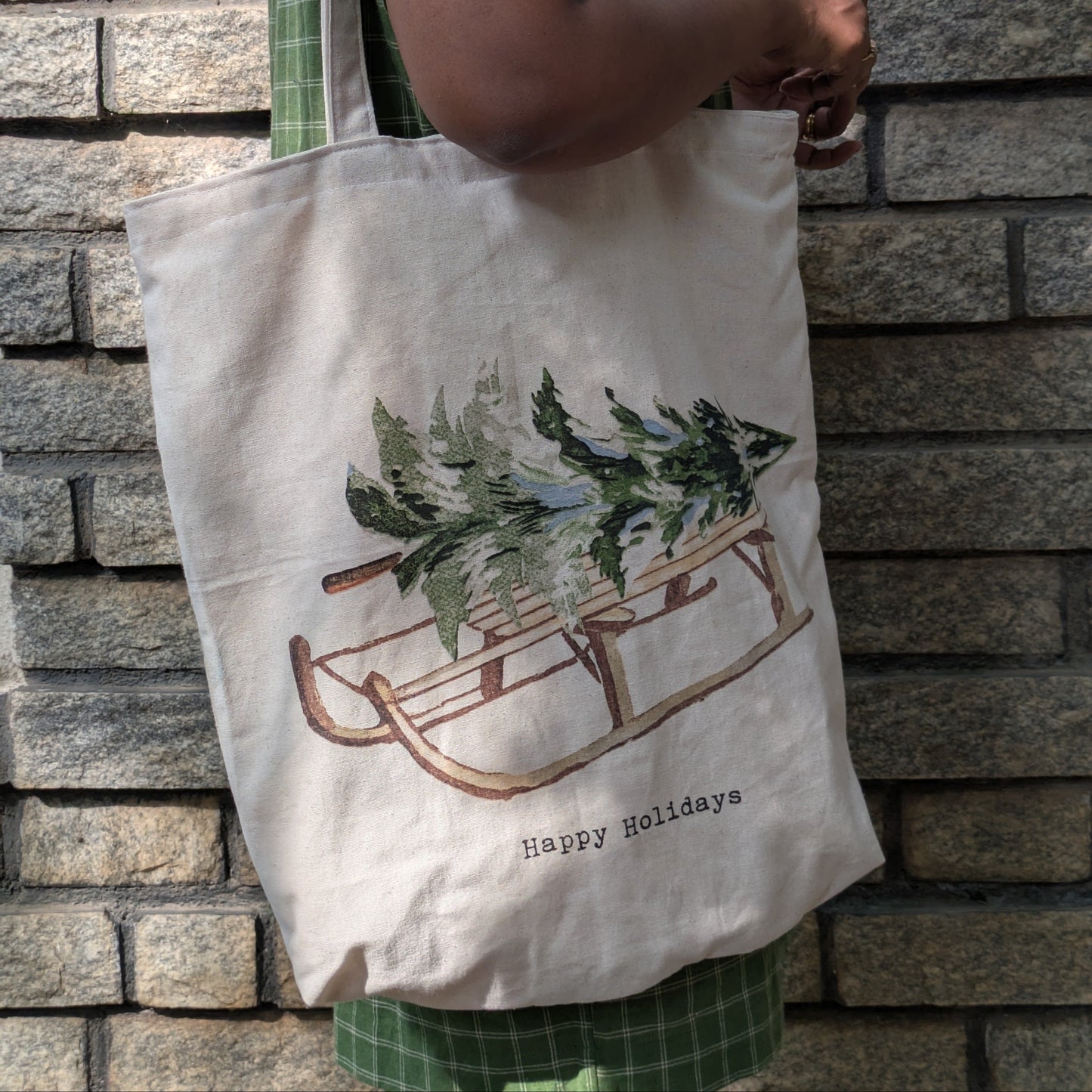 Person holding a tote bag with a Christmas design against a stone wall.