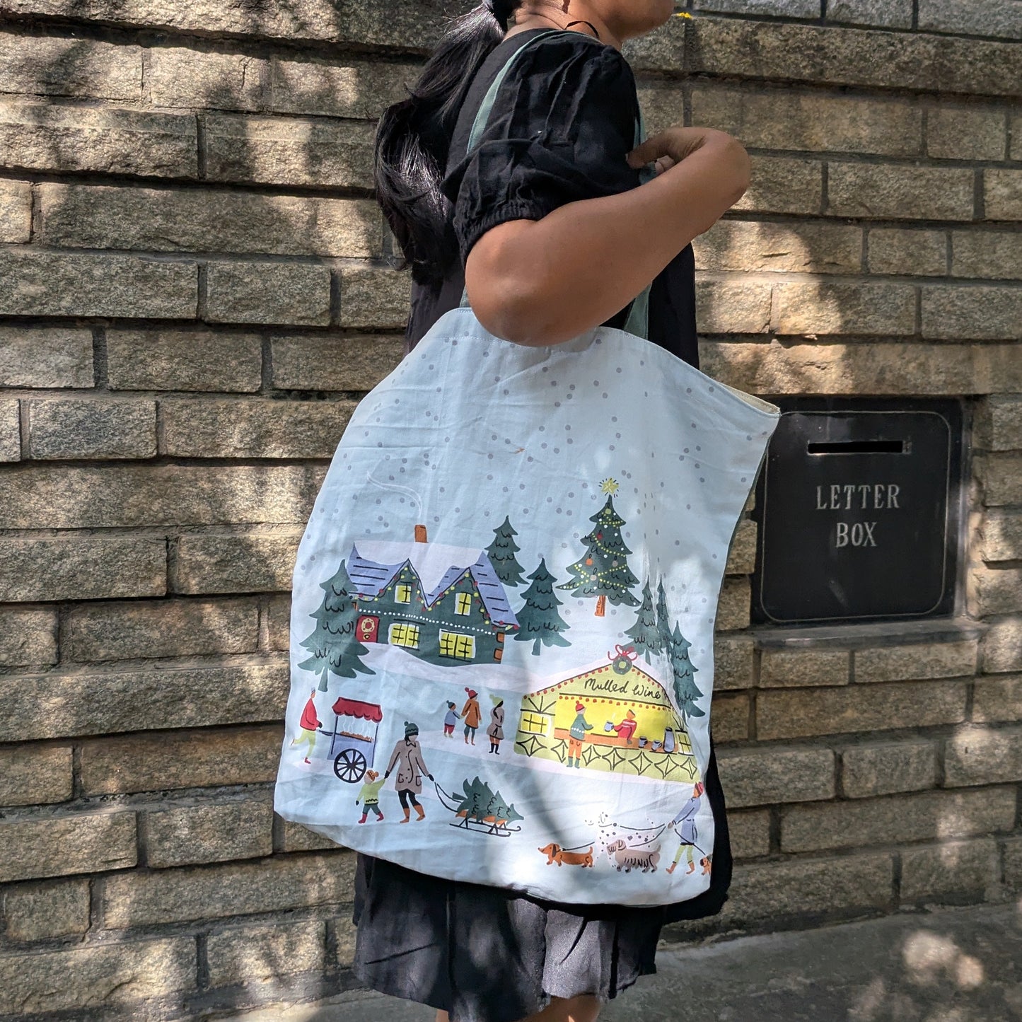 Person holding a tote bag with a colorful design against a brick wall.