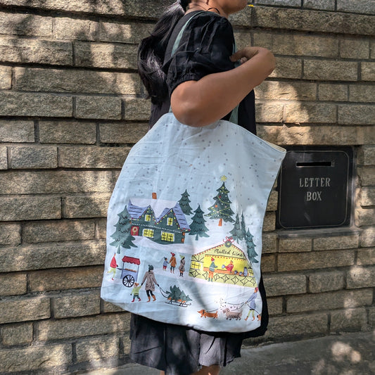 Person holding a tote bag with a colorful design against a brick wall.