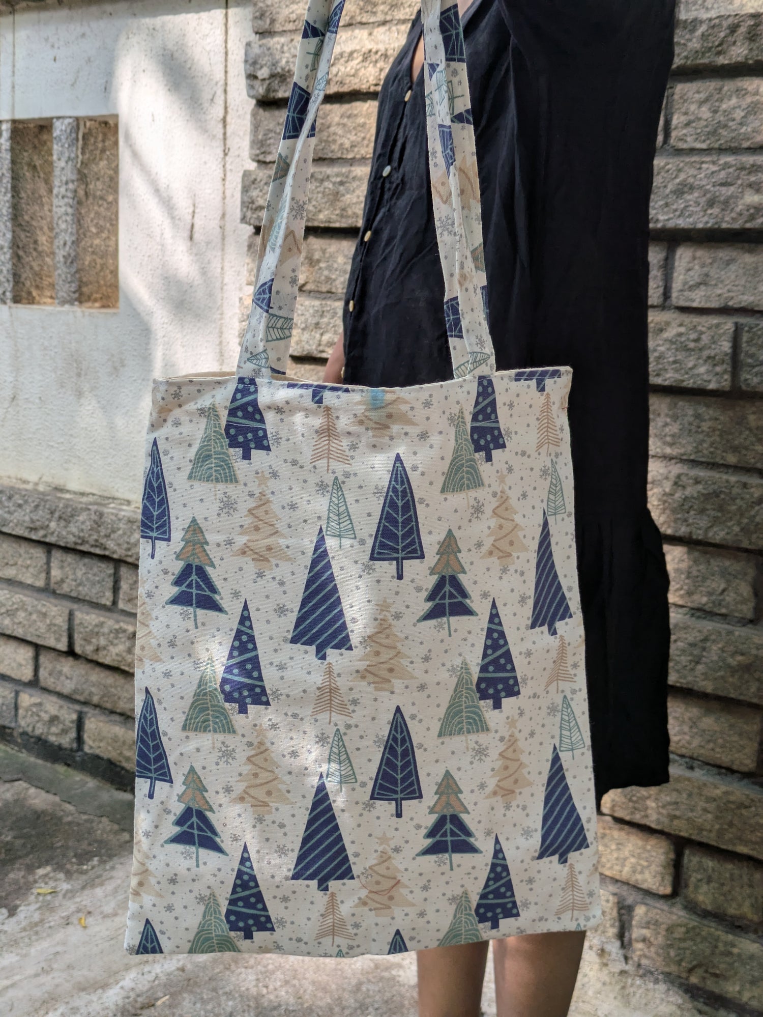 Tote bag with tree pattern held by a person against a stone wall.