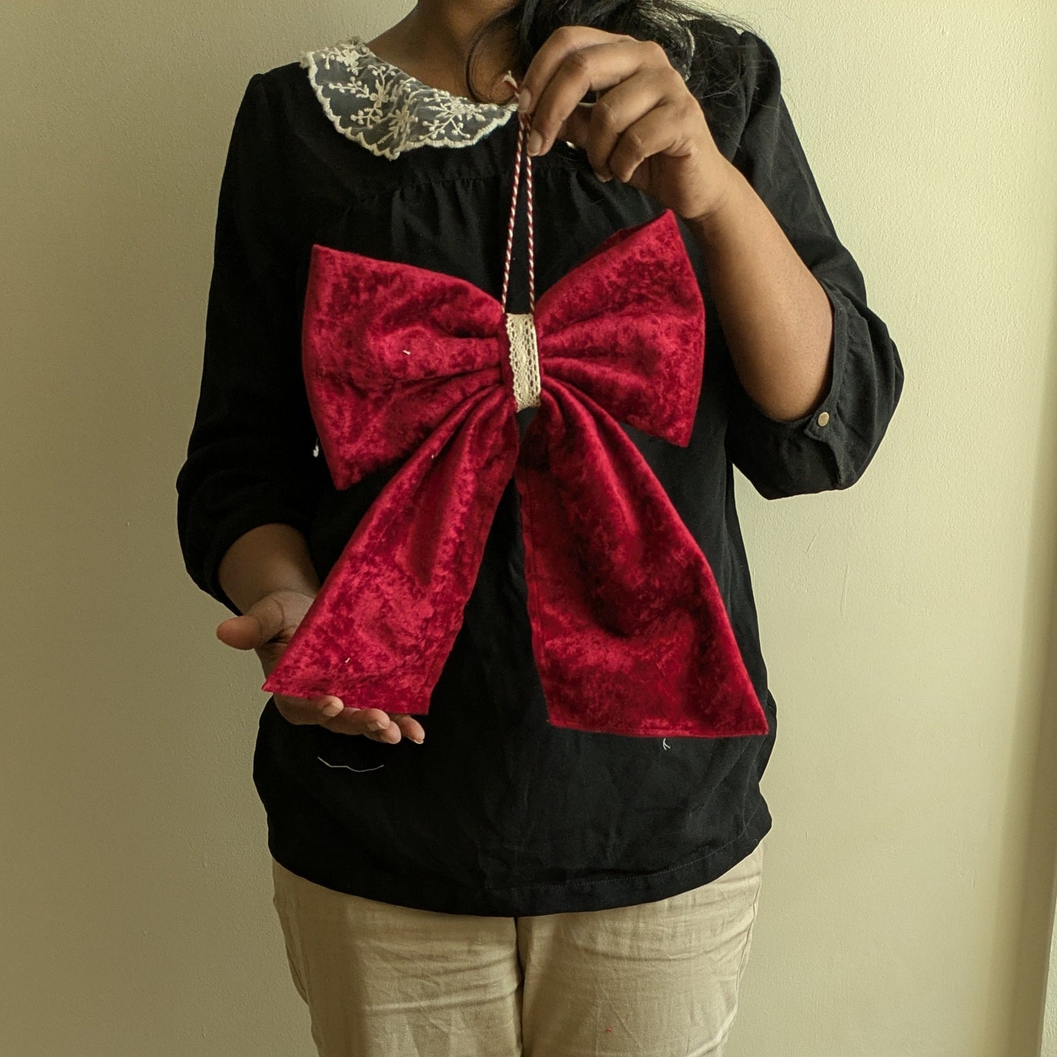 Person holding a red bow against a plain wall.