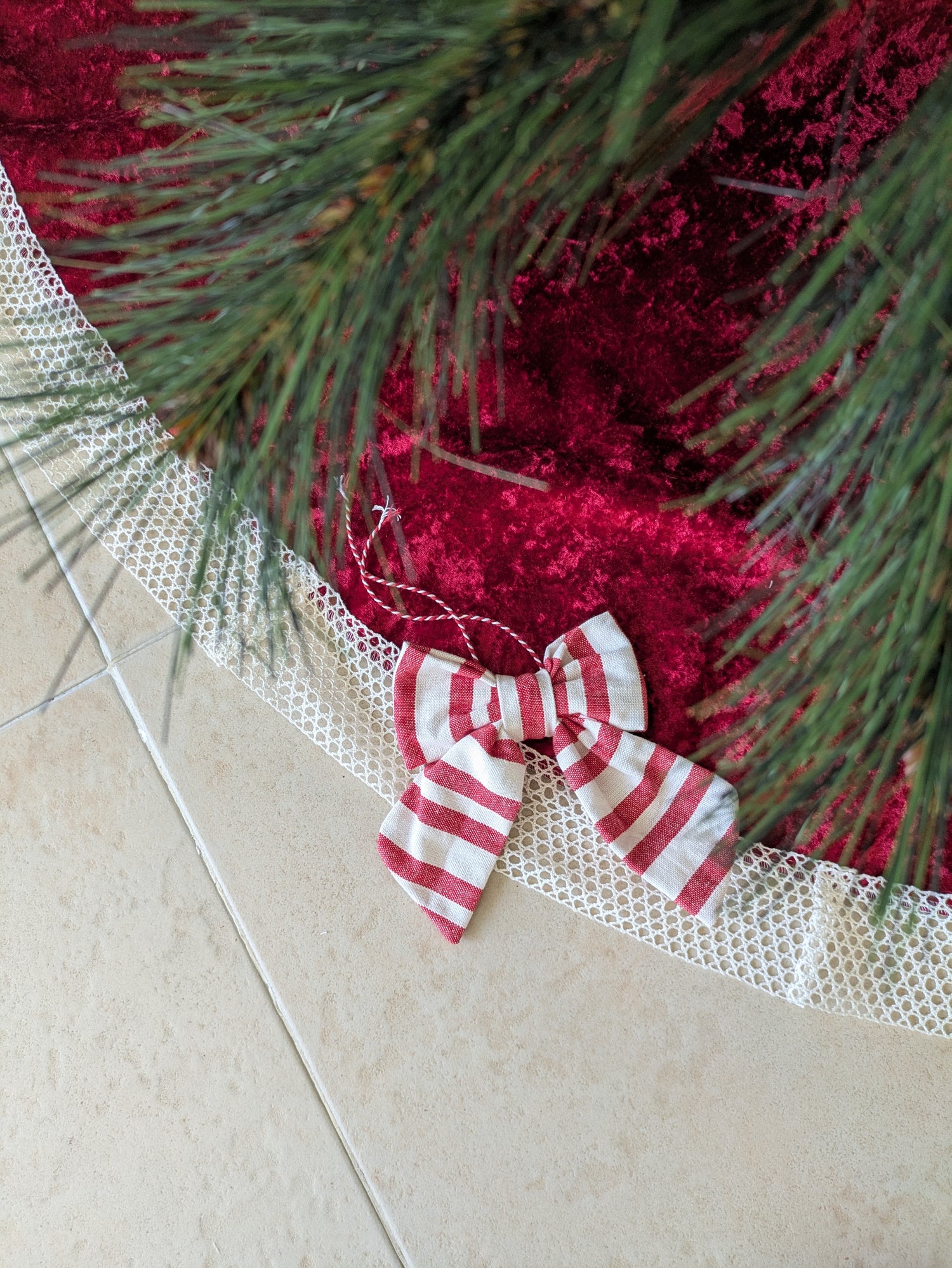 Red fabric with greenery and a red and white striped bow on a tiled floor.