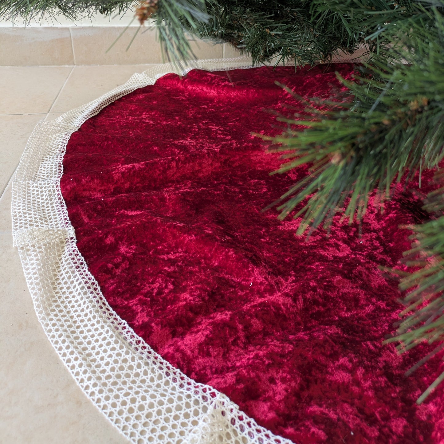 Red velvet tree skirt with white lace trim under a Christmas tree.