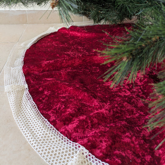 Red velvet tree skirt with white lace trim under a Christmas tree.