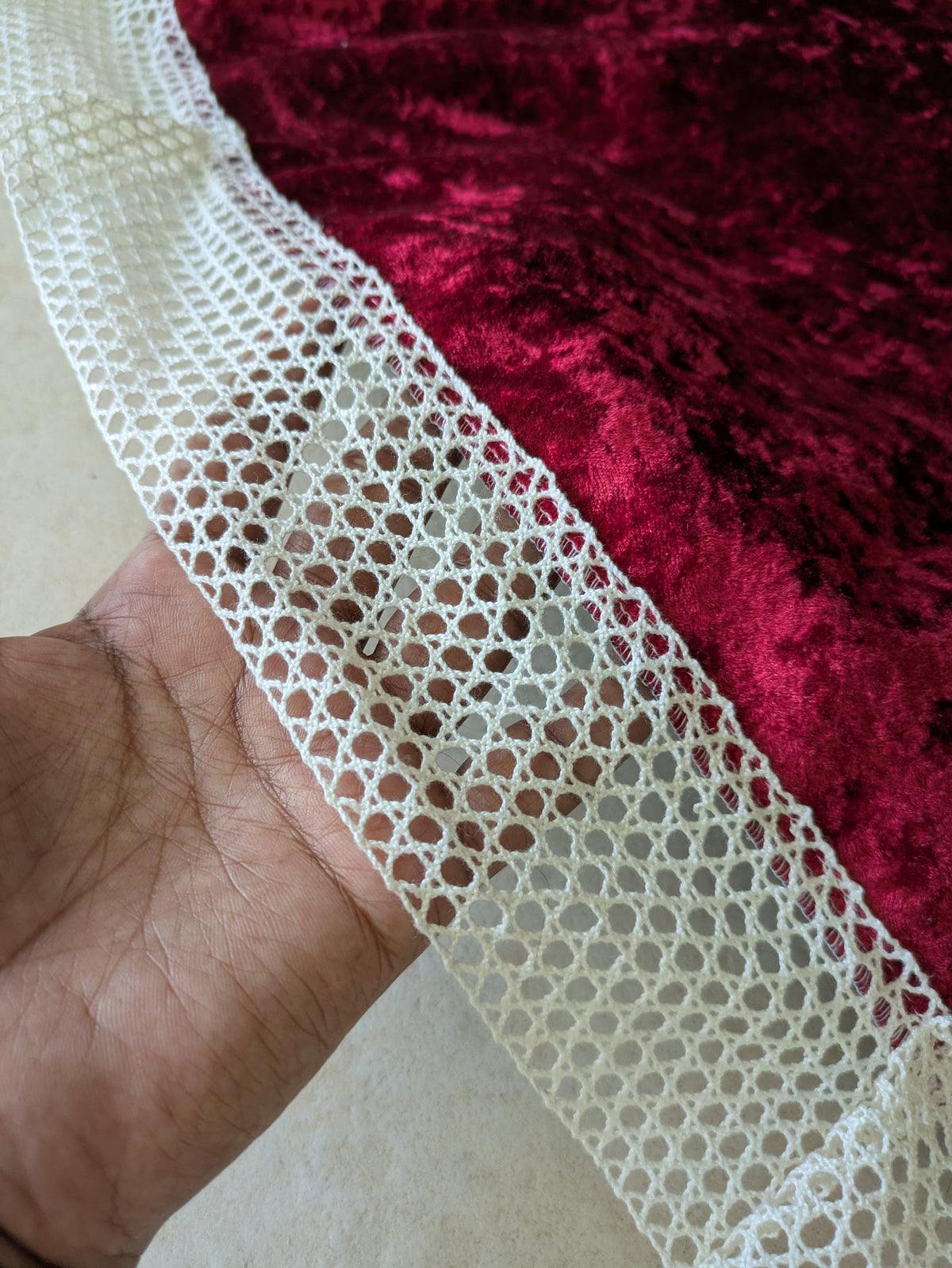 Close-up of a hand holding a strip of white lace fabric against a red textured background.