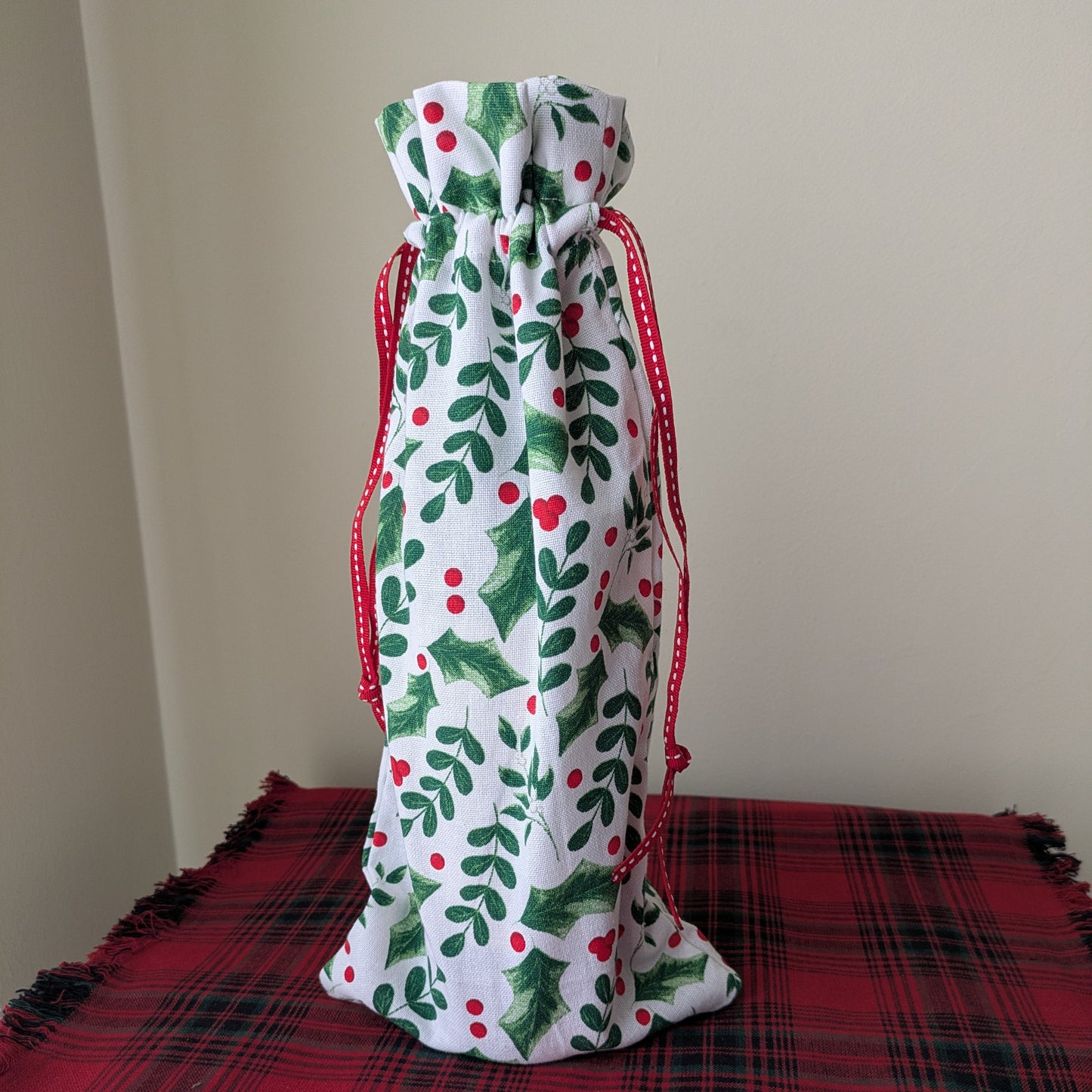 Decorative drawstring bag with holly design on a red plaid surface