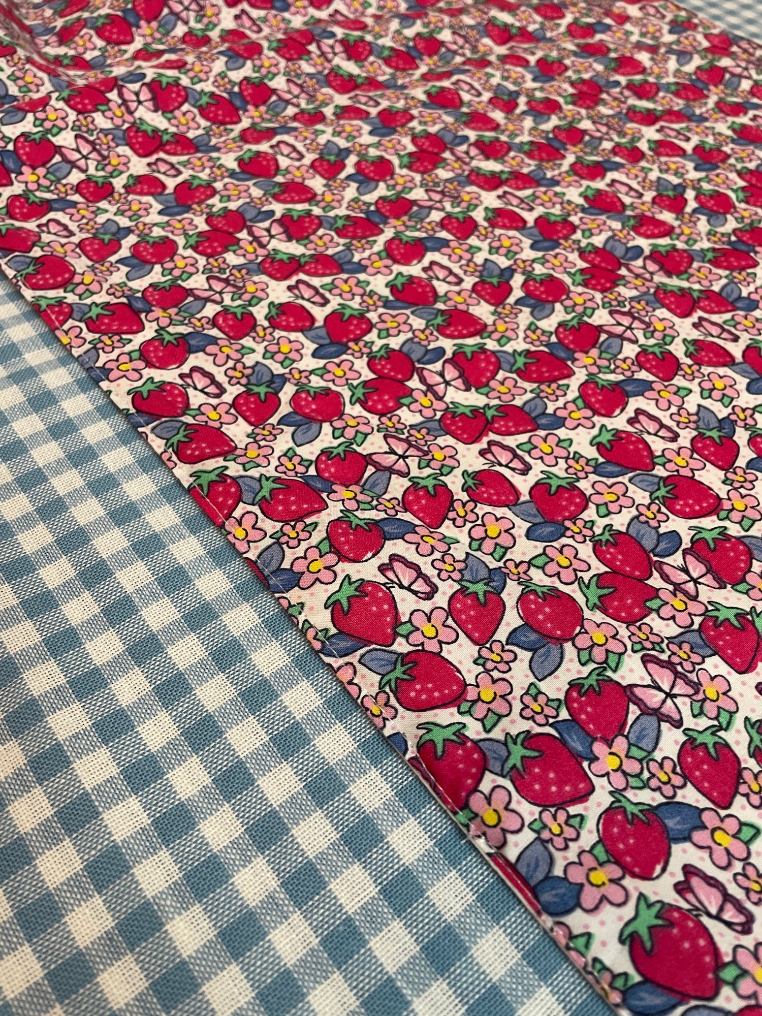 a table runner in summer colours, starawberry garden ditsy print all over and with frilly edges. styled against a light blue gingham table cover